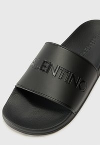 Sandală de cauciuc neagră cu talpă texturată și o curea lată, embosată, care afișează numele mărcii "VALENTINO". Finisaj neted.