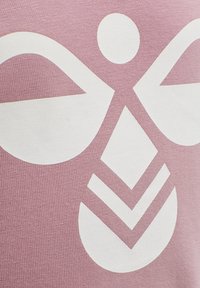 Rosa stof med et stort hvidt grafikdesign, der inkluderer abstrakte former: to afrundede vinger, en cirkel og diamanter.