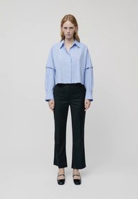 Ανοιχτό γαλάζιο πουκάμισο με ρίγες και φαρδιά μανίκια, συνδυασμένο με μαύρα κομμένα παν trousers και μαύρα επίπεδα παπούτσια. Απλή φόντο.