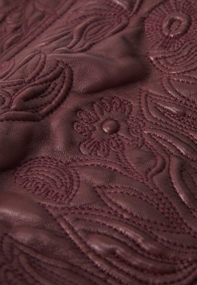 Burgundy embossed leather featuring intricate floral and wave patterns, with a textured surface and smooth, rounded stitching details.