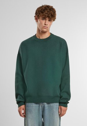 Dark green knit sweater with a crew neckline, dropped shoulders, and ribbed cuffs and hem. Paired with light blue denim jeans.