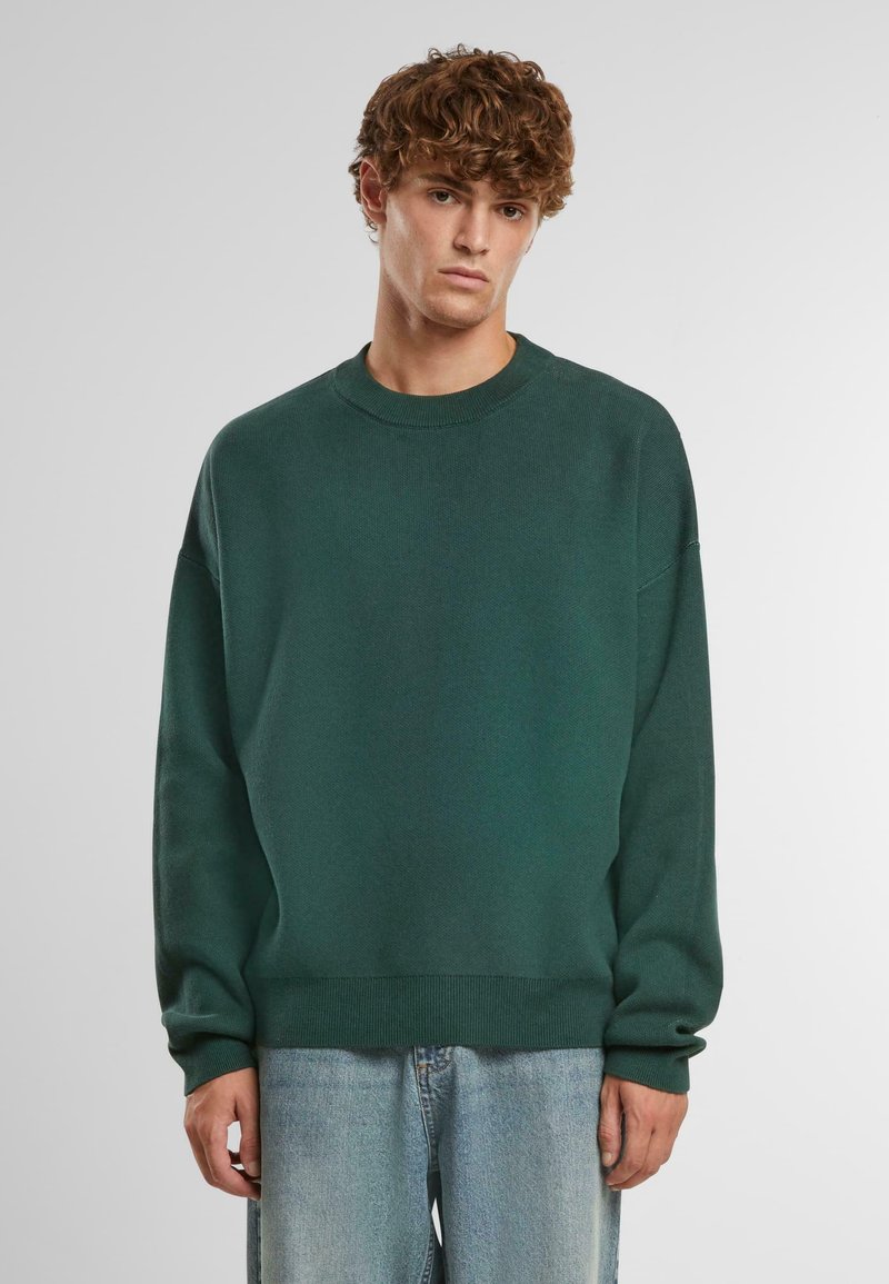 Pulover tricotat verde închis, cu necklines de tip crew, umeri căzuți și mansete și tiv cu nervuri. Asortat cu blugi din denim bleu deschis.