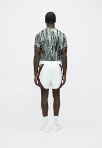 Īsroku krekls ar melnu un baltu viļņveida rakstu, kopā ar baltām šortām ar vīnsarkaniem un zaļiem akcentiem. Izskatu papildina baltas sporta kurpes.