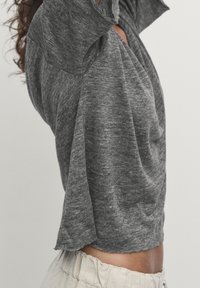 Szary, krótki rękaw, luźny top z teksturowanej tkaniny i zaokrąglonym dołem. Charakterystycznym elementem jest złożony kołnierz.