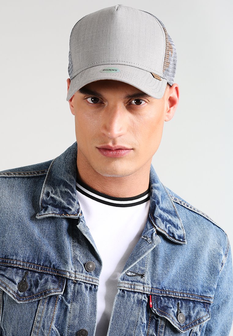 Gorra gris con un frente de tela texturizada y parte trasera de malla; presenta un logo verde y un visera curvada. Llevada con una chaqueta de mezclilla y una camisa blanca.