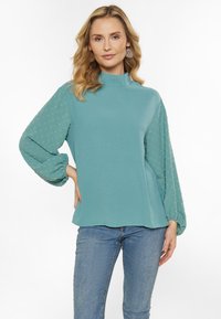 Bluemarin, bluză cu mânecă lungă și guler înalt. Corp neted și mâneci bufante texturate cu modele cu puncte mici. Design casual, cu o croială lejeră.