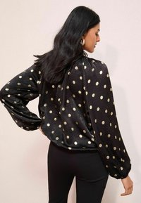 Mustmustärgne pluus, millel on kuldsed täpid, pikad puhvärved ja ümmargune ääreline. Kangas on sile ja kergelt tekstuuriga.