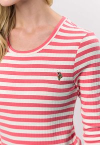 Roosa ja valge triibuline pika varrukaga särk soonilise tekstuuri ja ümarate kaelusega. Vasakul rinnal on väike tikitud muster.