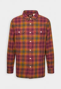 Chemise en flanelle à manches longues avec des boutons, présentant un motif à carreaux multicolores en orange, violet, vert et jaune, dotée de deux poches poitrine devant.