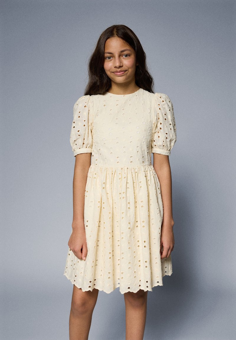 Robe en coton jaune pâle avec des manches volantes, motif en œillets, taille froncée et ourlet festonné. Texture lisse avec des découpes décoratives.