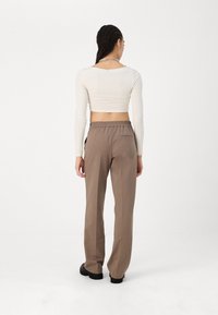 Dlouhý rukáv, krémový crop top v kombinaci s volnými hnědými kalhotami se širokým elastickým pasem. Hladký povrch, minimalistický design, žádné viditelné vzory.