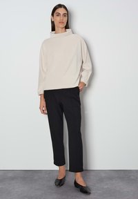 Licht beige top met een kraag, losse pasvorm; gecombineerd met op maat gemaakte zwarte pantalon en zwarte ballerina's. Glad textuur, minimalistisch ontwerp.