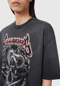 Zwart katoenen t-shirt met een grote afbeelding van slangen en schedels in grijs en rood, voorzien van een ronde hals en korte mouwen.