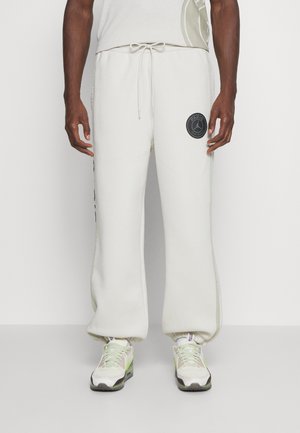 Lys beige sweatpants med snoretræk i taljen, sidelommer og et sort cirkulært logo på venstre lår. Blød tekstur og afslappet pasform.