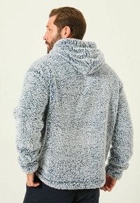 Flauschiger grauer Kapuzenpullover mit plüschiger Textur, der eine große Kapuze, lange Ärmel und eine lockere Passform aufweist. Betont durch ein gemütliches Erscheinungsbild.