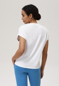 Hvit kortermet t-skjorte med rund hals, kombinert med blå bukser. Stoffet ser mykt ut med en jevn tekstur og en avslappet passform.