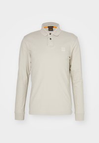 Beige polo shirt met lange mouwen, een placket met twee knopen, subtiele merkl logo op de borst en contrasterende oranje binnenkant van de hals.