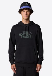 Black hoodie featuring a front pocket and hood, adorned with a green outlined logo. Worn with a black and blue bucket hat.