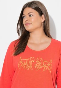 Rotes Langarmshirt mit rundem Ausschnitt und einem gelb umrandeten Motiv von zwei Hunden auf der Vorderseite. Weiche Textur und entspannte Passform.