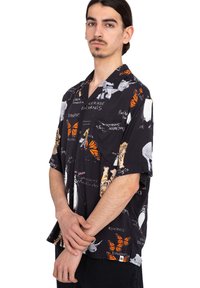 Camisa de manga corta negra con un estampado de mariposas y animales en múltiples colores, y texto en blanco. Hecha de una tela ligera con un corte relajado.