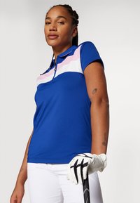 Polo shirt da donna di colore blu con colletto zip, caratterizzato da strisce orizzontali rosa e bianche sul petto. Tessuto liscio e leggero.