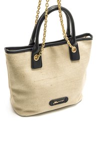 Bolso tote de lona beige con detalles en cuero negro, asas de cadena dorada y placa con el logo. Presenta una textura suave y una forma estructurada.