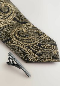 Schleife in schwarz mit kompliziertem goldenen Paisleymuster. Begleitet von einer grafischen silbernen Krawattennadel mit gerippter Textur.