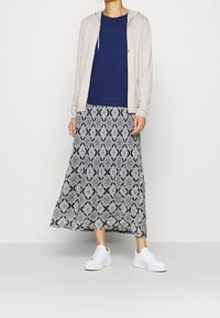 Felpa beige chiaro, t-shirt blu navy e una lunga gonna a fantasia con disegni blu, bianchi e neri, abbinata a sneaker bianche.