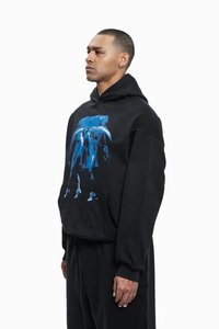 Sort hoodie lavet af blødt stof, med et blåt grafikdesign på fronten, kengurulomme og hætte med snor.