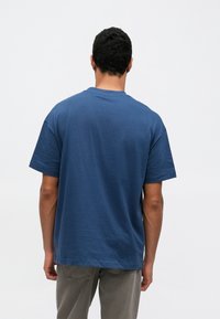 Κοντομάνικη μπλούζα από μονόχρωμο βαμβάκι σε σκούρο μπλε χρώμα. Σχεδίαση με λαιμόκοψη τύπου crew, άνετη γραμμή και λεία υφή, εμφανιζόμενη από πίσω.