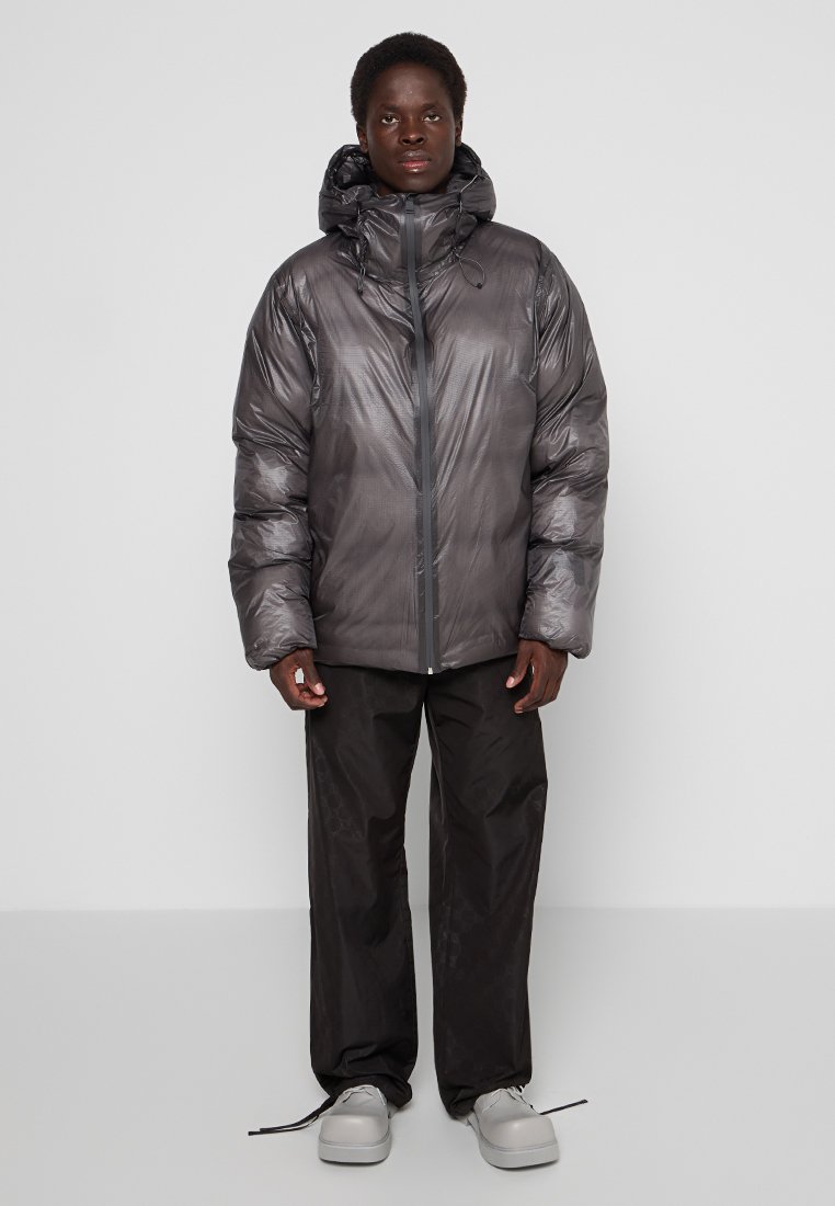 Giacca a vento in grigio metallizzato, con colletto alto, chiusura a zip e cappuccio. Abbinata a pantaloni neri e sneaker grigie per creare contrasto.