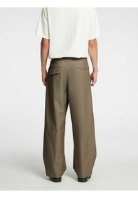 Brūnas platām biksēm ar teksturētu audumu, augstu jostasvietu un divām kabatām aizmugurē. Valkātas ar īsām piedurknēm baltu kreklu.