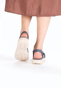 Donkerblauwe sandaal met een beknopte beige zool, voorzien van verstelbare banden en een gestructureerde inlegzool, gezien vanuit de achterkant.