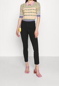 Kortärmad stickad topp med pastellfärgad zigzag- och rutmönster, i kombination med svarta tighta byxor med knappdetalj. Lila sandaletter med remmar; liten gul väska.