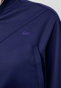 Felpa navy con colletto con zip, in tessuto strutturato e con un discreto logo ricamato a forma di coccodrillo sul petto.