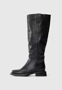 Bota alta de couro preto com salto baixo e empilhado, bico redondo e uma alça de puxar com a gravação "SL" no lado externo, perto do topo.