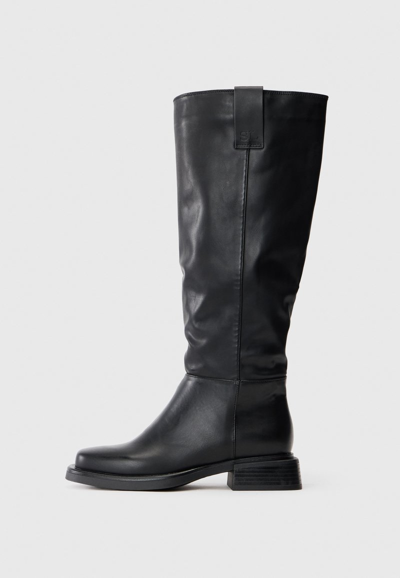 Pitkä musta nahkasaapas, jossa on matala pinoheeli, pyöreä kärki ja vetotappi, johon on kohokuvioitu "SL" ulkopuolelle lähellä ykköstä.