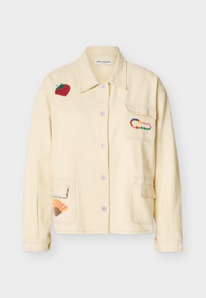 Κρεμ σακάκι με κουμπιά, με επιδιορθωτική ετικέτα φράουλας στον ώμο, πολύχρωμη καρφίτσα με χάντρες στην τσέπη του στήθους και επιδιορθωτική ετικέτα ανεμιστήρα στην κάτω τσέπη.