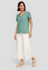 Miętowa koszulka z dekoltem w serek i krótkim rękawem w połączeniu z szerokimi spodniami w kolorze kremowym oraz beżowymi sandałami na koturnie z plecionymi paskami.