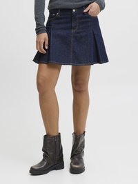 Denimska krilo ima razširjen dizajn, temno pranje in kontrastno šivanje. Nošena z ohlapnimi rjavimi usnjenimi gležnjarji.