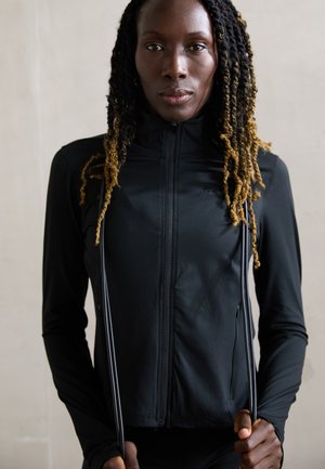 Black fitted zip-up athletic jacket with long sleeves, textured surface, and two drawstrings held by the model. Smooth fabric with logo detail.