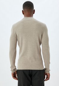 Beige geribbelde lange mouwen trui met een ronde hals en aansluitende manchetten. De stof heeft een zachte textuur, wat zorgt voor een figuurvolgende silhoeet.