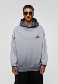 Grijze gradient hoodie met een grote capuchon, geribbelde zoom en manchetten. Voorzien van geborduurde tekst "Stay Moment" op de borst. Gemaakt van zachte stof.