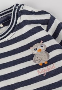 Langärmliges, gestreiftes Shirt in Marineblau und Weiß mit gesticktem Eulenmotiv, orangefarbener Schnabel und zarten Akzenten in Pfirsichfarbe, sowie Druckknopfverschlüssen am Hals.