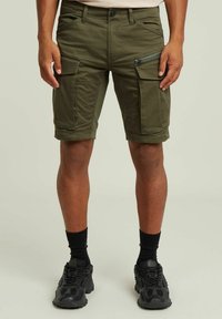 Pantaloni cargo verde oliva con molte tasche, dettagli con zip e risvolti. Realizzati in tessuto resistente, caratterizzati da una chiusura con bottone.