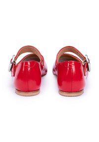 Chaussures en cuir rouge avec finition laquée, bout arrondi et une bride de cheville réglable avec une boucle en argent. Semelle plate et texture lisse.