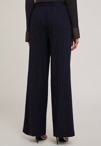 Marineblauwe wijde pantalon met lichte streepjes, van op maat gemaakte stof, een strakke tailleband en een subtiele glans. Heeft een hoge taille en is volledig lang.