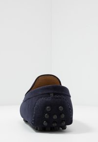 Marineblå ruskindsmokkasiner med afrundet hæl, kontrastsy nær og gummistænger på ydersålen for godt greb. Enkel bagdesign med lav profil.