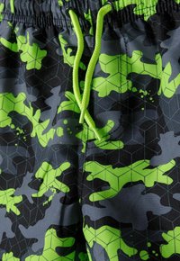 Shorts de bain camouflage avec un motif géométrique en noir, gris et vert fluo. Comprend une taille avec cordon de serrage et un tissu lisse et texturé.