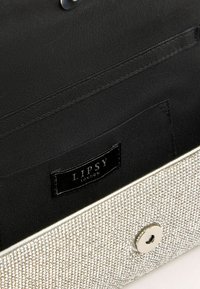 Interno in tessuto nero di una pochette argentata scintillante con un bottone magnetico e un'etichetta "Lipsy London" all'interno.